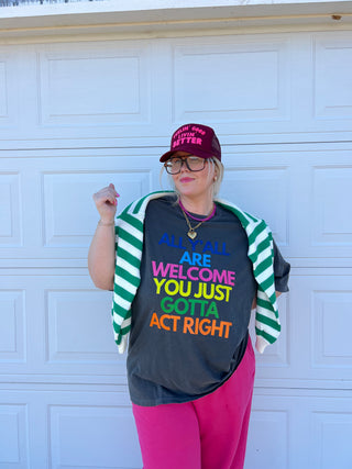 Person wearing a colorful shirt with text and a striped sweater, standing against a white door.
